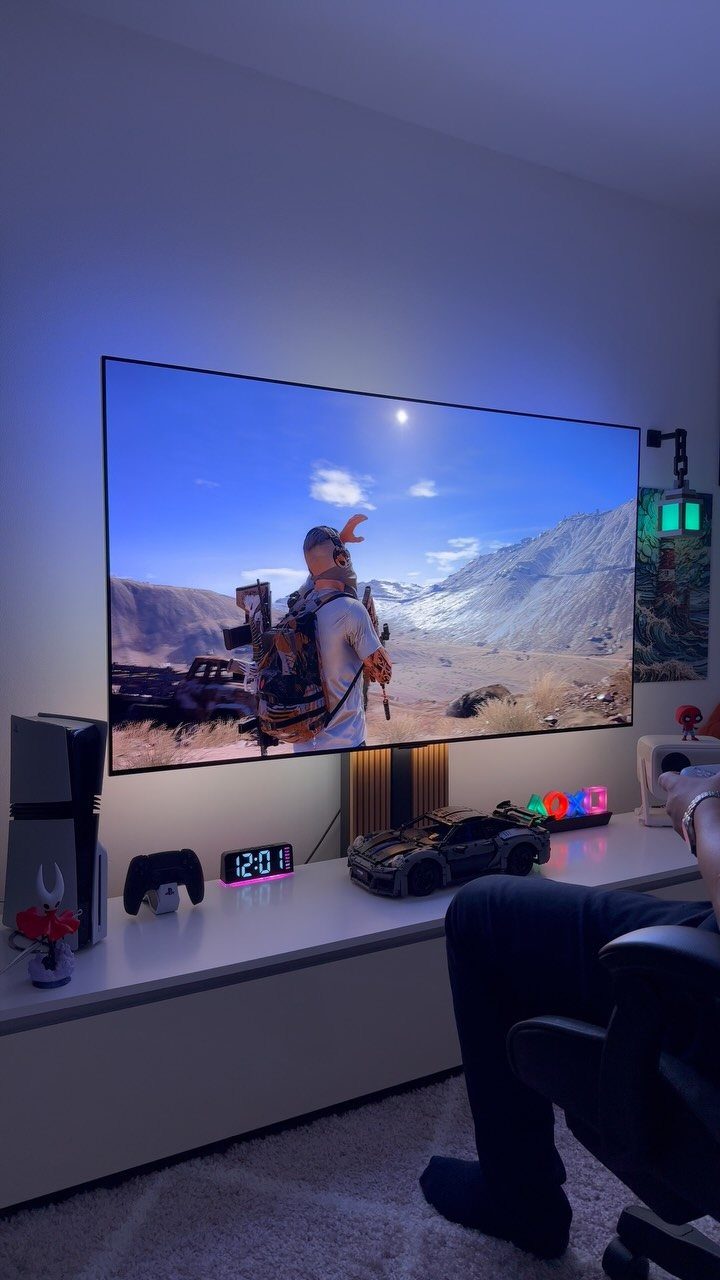 Mounted television displaying a video game with a console and accessories on a white table.