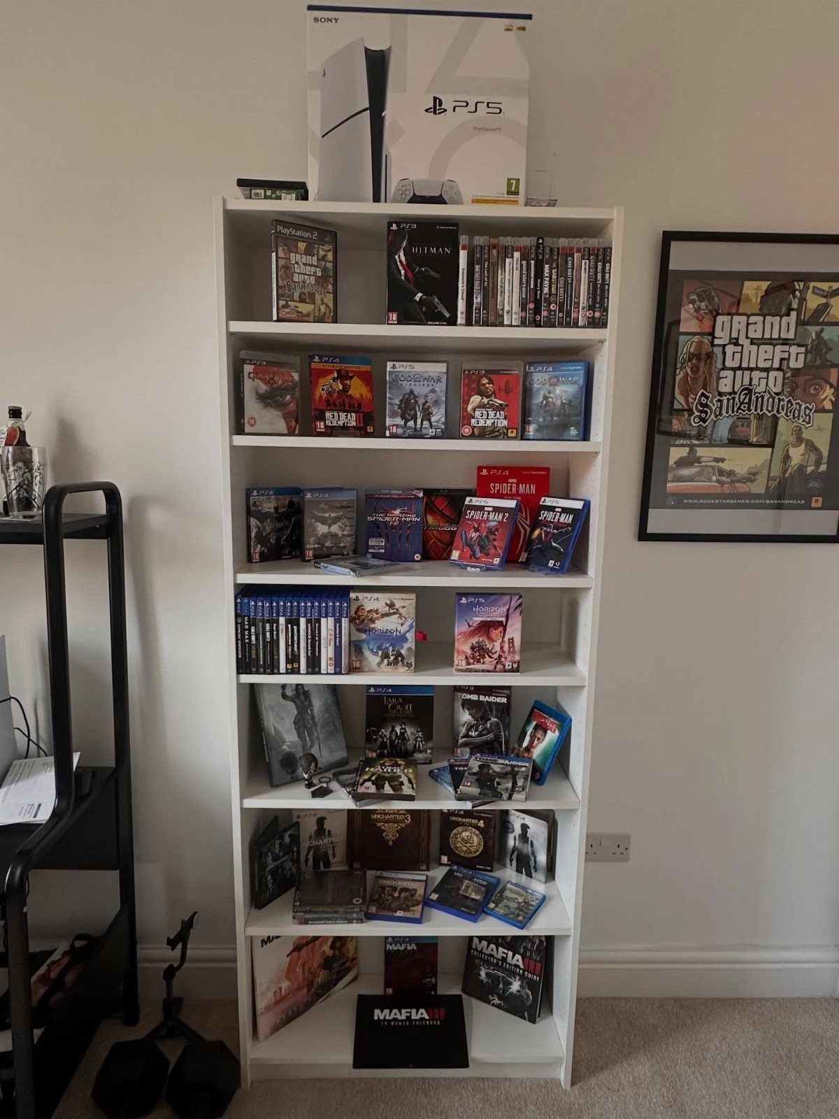 White bookshelf filled with video games and a PS5 box against a white wall.