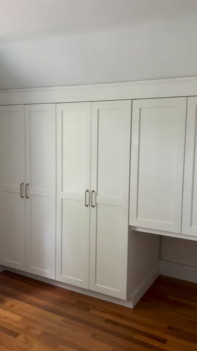 White built-in cabinets with silver handles reaching from hardwood floor to white ceiling.