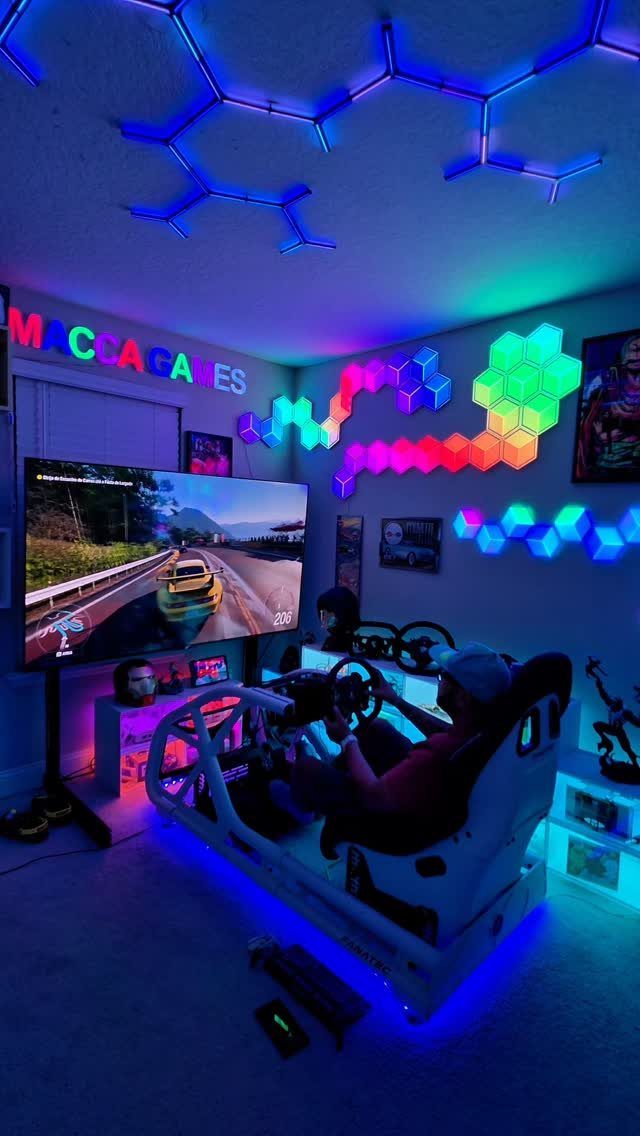 Gaming room with racing simulator, large screen, and colorful neon hexagonal wall lights.