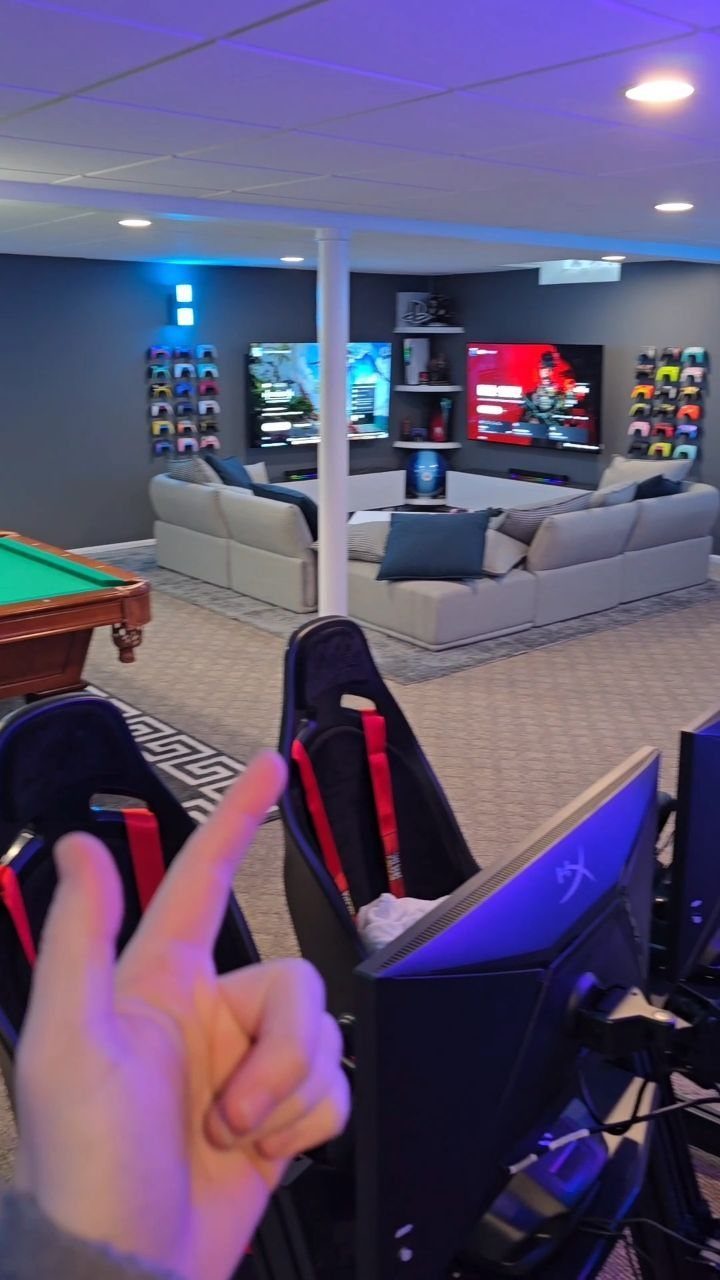 Pool table and gaming chairs in a modern basement man cave with purple lighting.