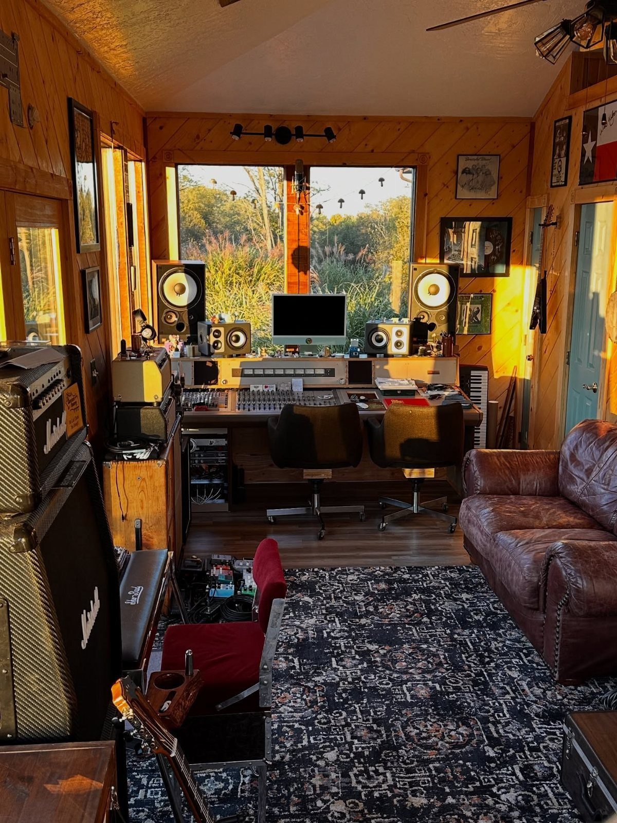 Music studio with mixing console, studio monitors, leather sofa, and wood-paneled walls.