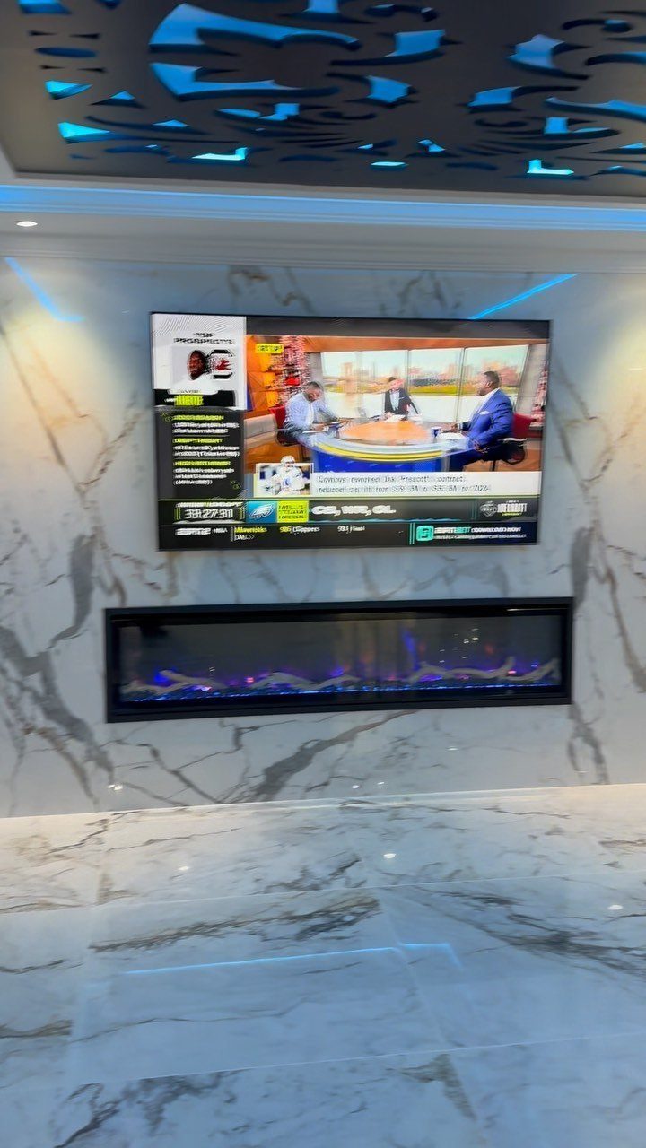 Modern living area with marble walls, a wall-mounted TV, and a blue electric fireplace.