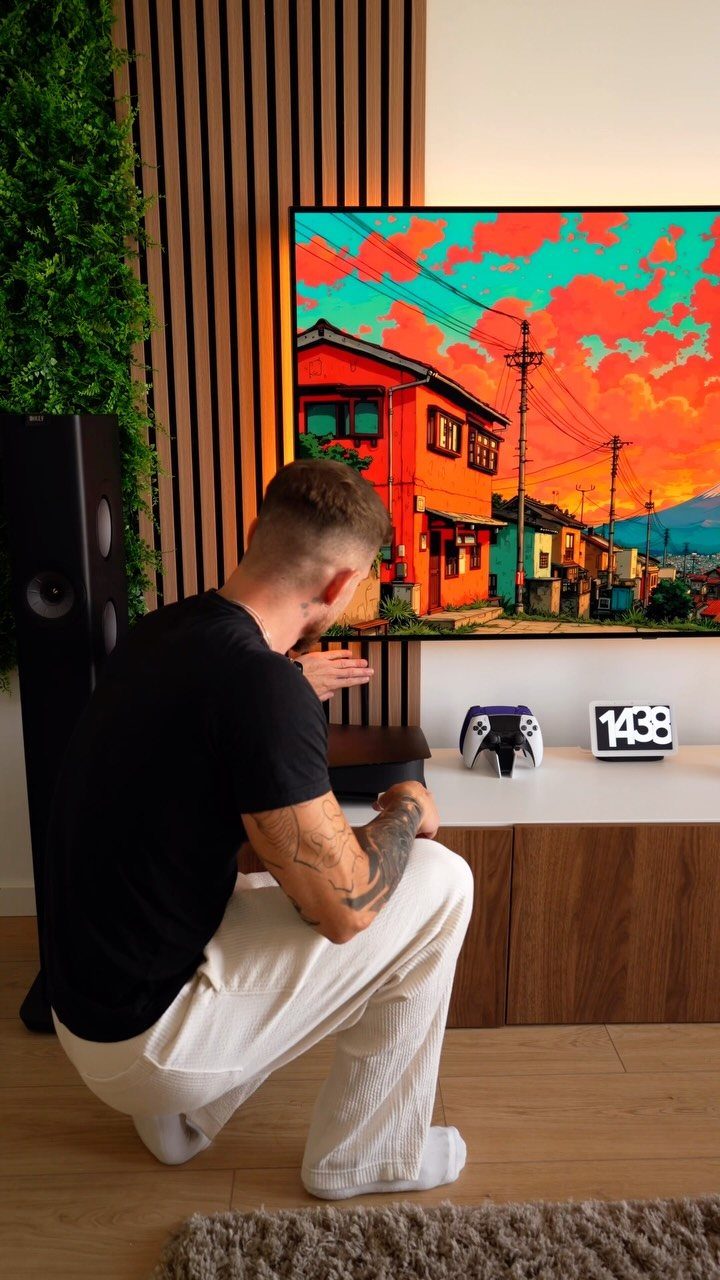 Man squatting in front of a large television in a modern gaming room.