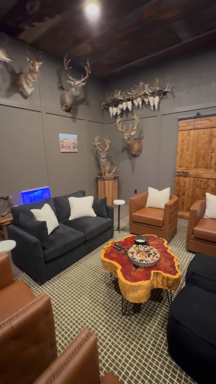 Rustic lounge with mounted deer trophies, leather chairs, and a live-edge wood table.