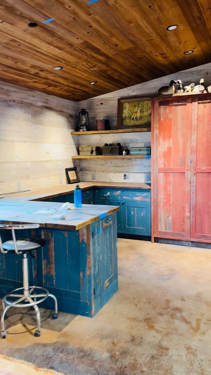 Rustic room with blue distressed island, red vintage cabinet, and wooden ceiling.