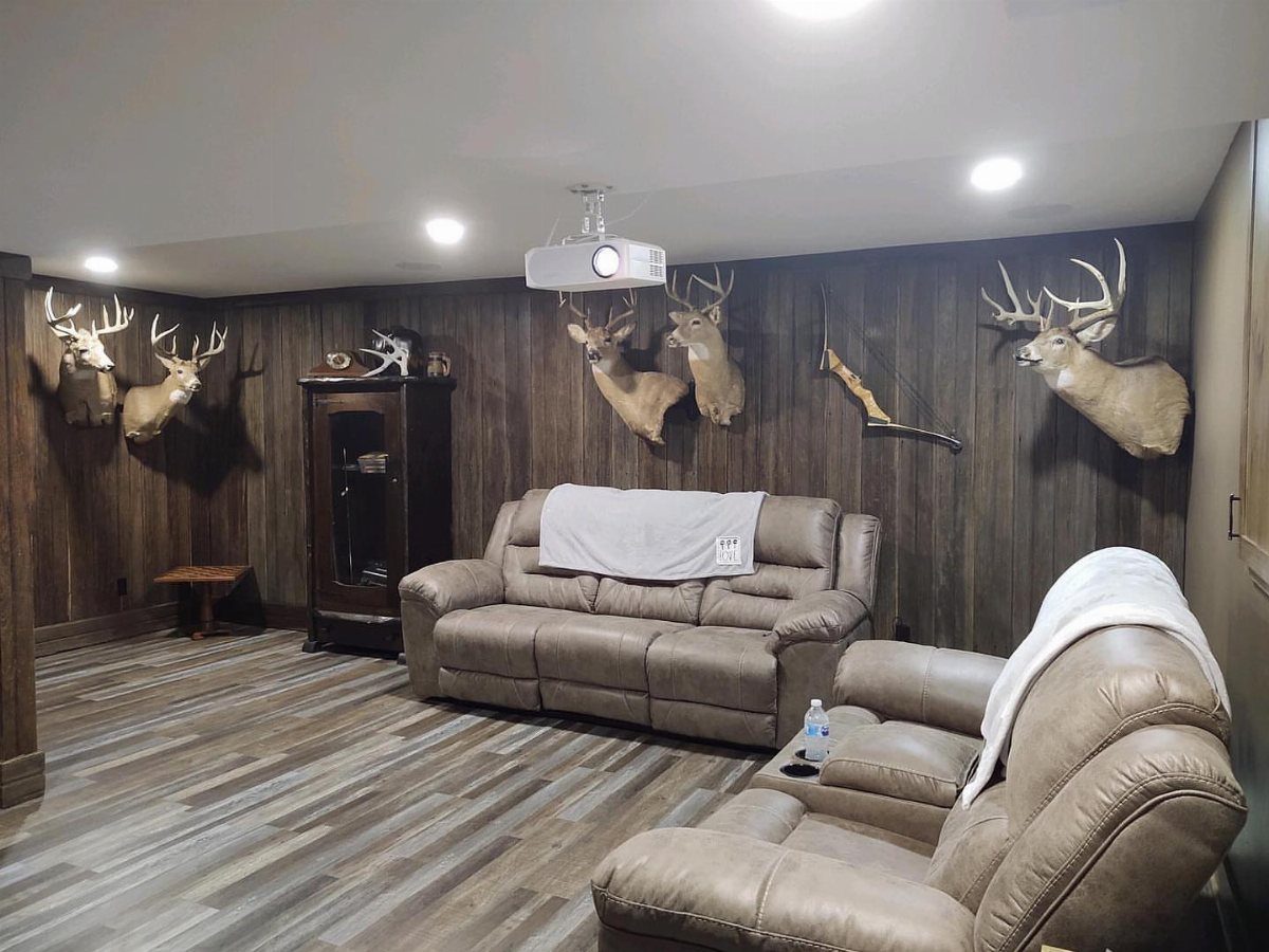 Deer head trophies mounted on grey wood walls in a rustic basement lounge.