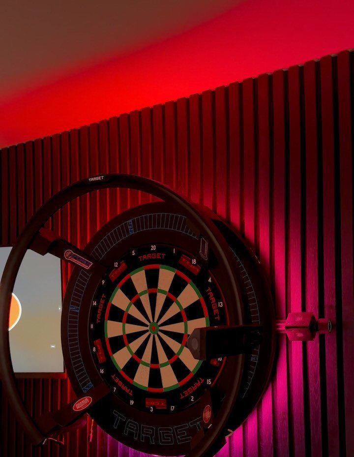 11 Man Cave Must Haves for Your Space 4 Dart board with protective ring mounted on a slatted wall with red lighting.