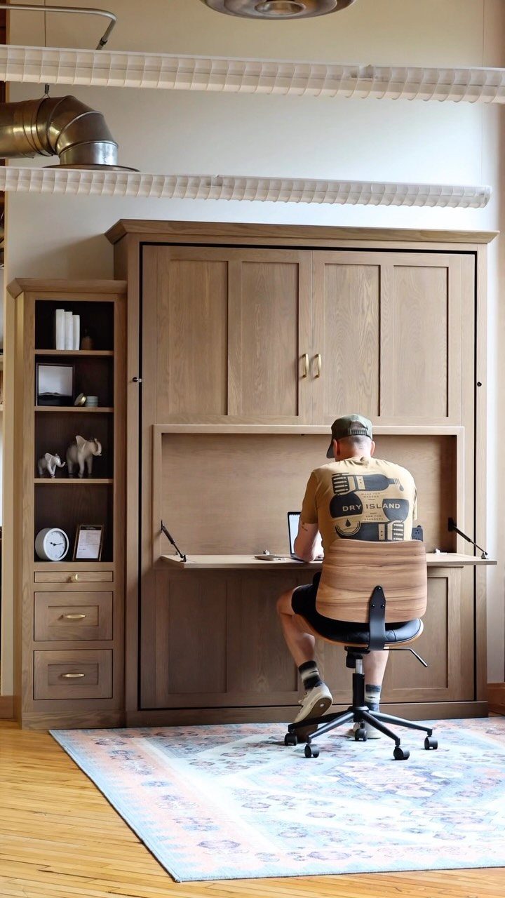 Man working at a desk integrated into a wooden murphy bed wall unit.