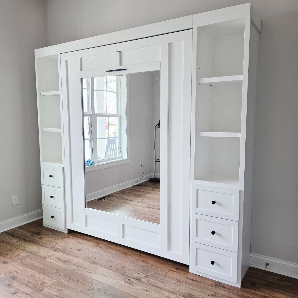 White Murphy bed with mirrored center and integrated side shelves and drawers.
