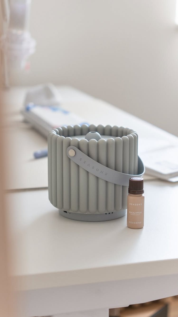 Grey ribbed essential oil diffuser and a small bottle on a white desk.