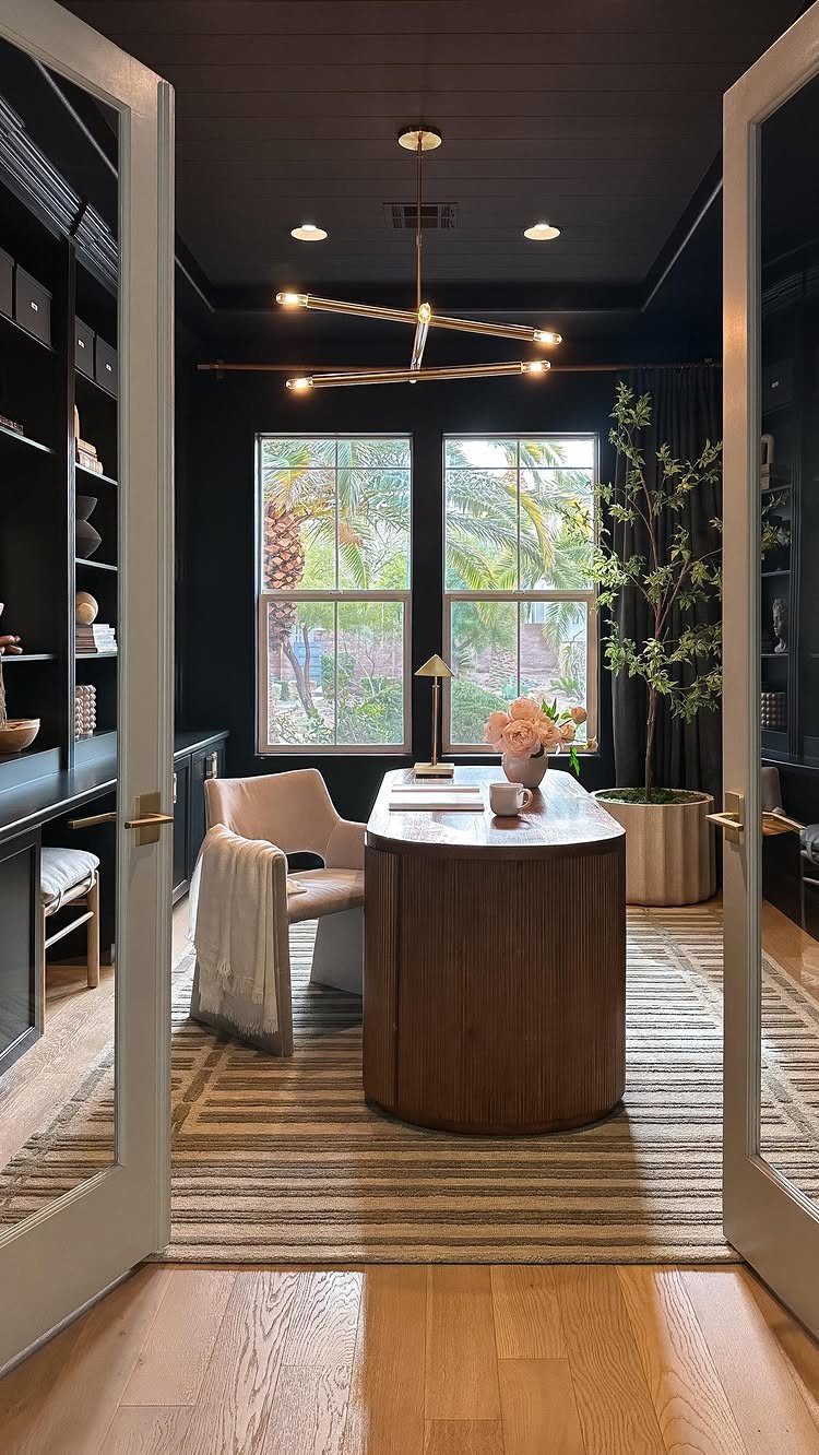 Home office with black walls, curved wooden desk, and modern gold ceiling light.