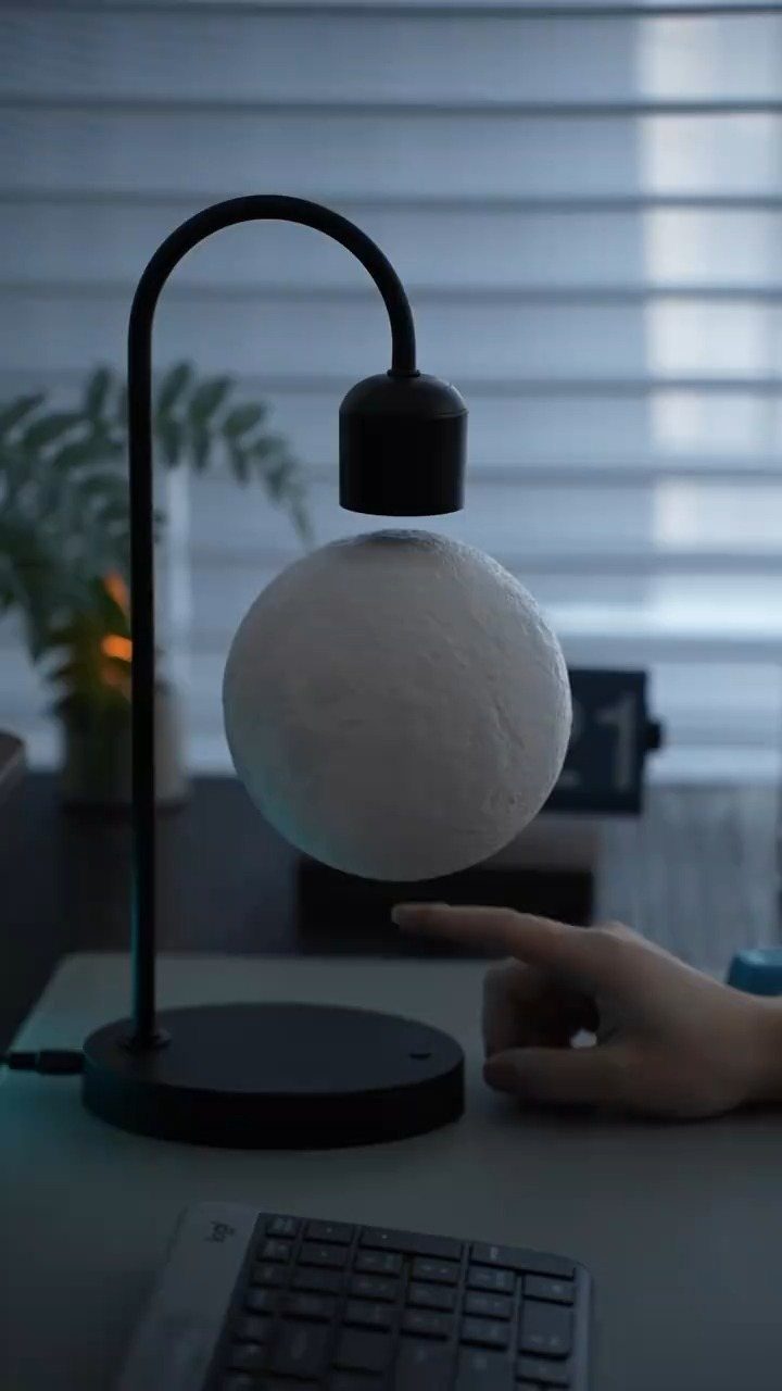 Levitating moon desk lamp glowing on a workspace with a hand nearby.