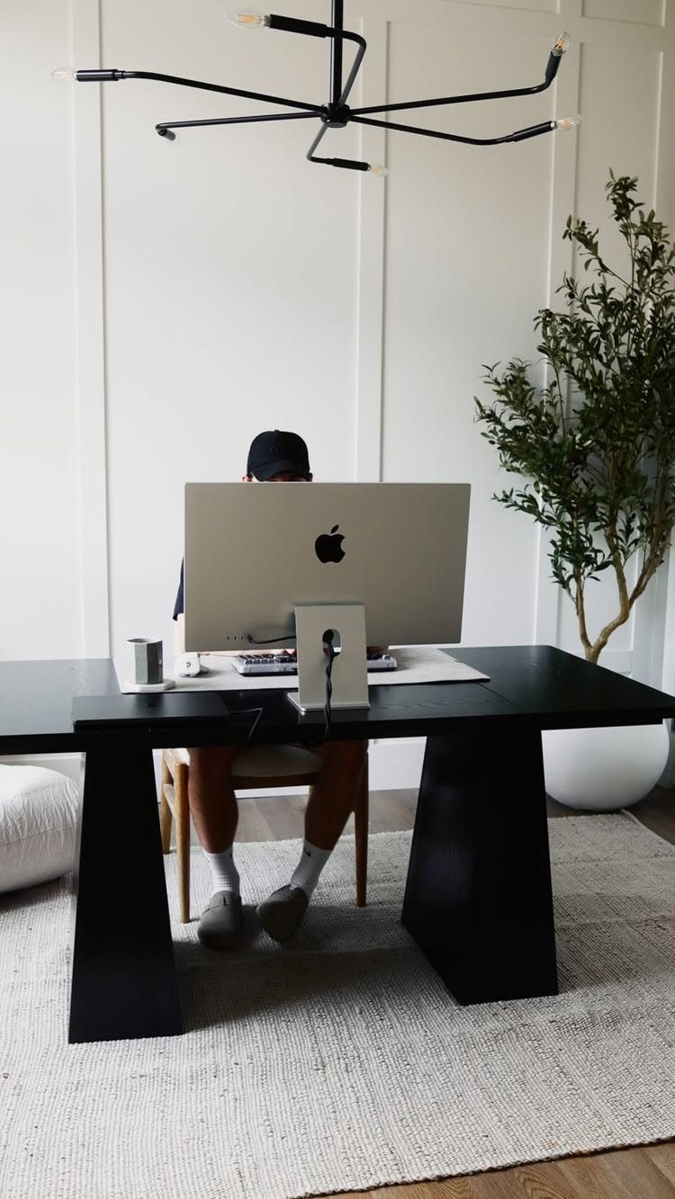 Modern minimalist home office with a black desk, silver monitor, and white walls.
