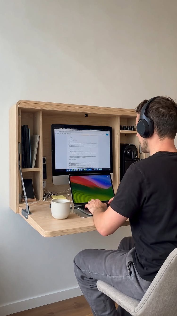 Man working at a wall-mounted foldable light wood pop-up desk with computer monitor.