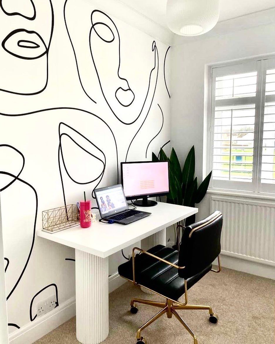 White home office desk with a black leather chair and line-art wallpaper