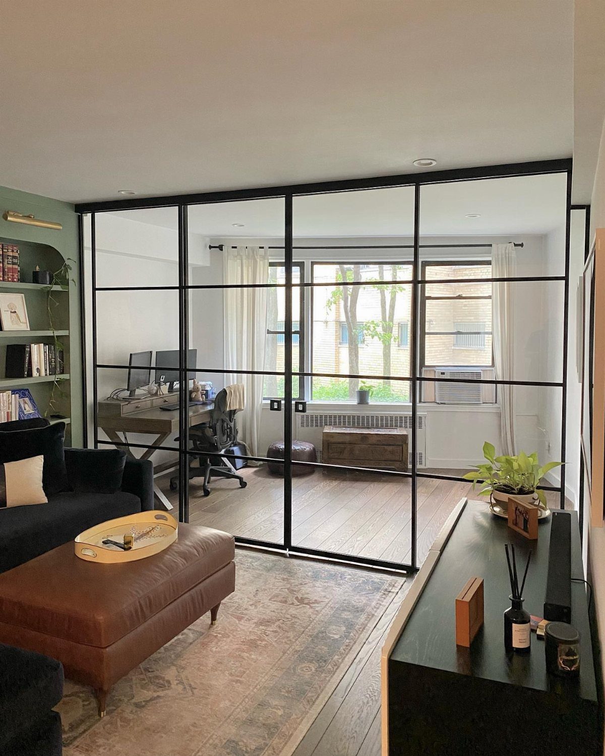 Black-framed glass wall partition separating a home office from a living room area.
