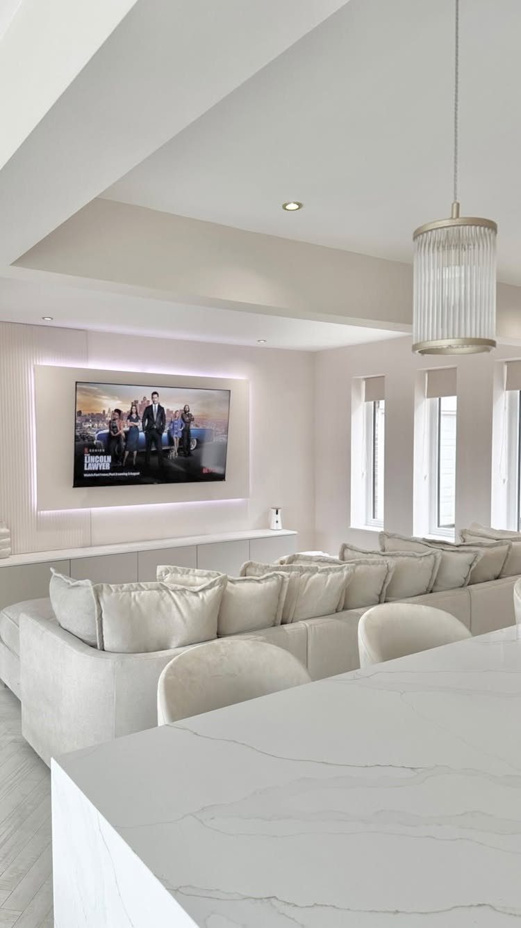 Recessed television with backlighting on a white wall above a long floating console.
