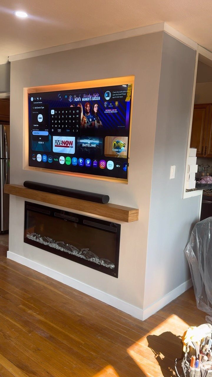 Recessed TV with orange backlight and a floating oak mantel above a fireplace.