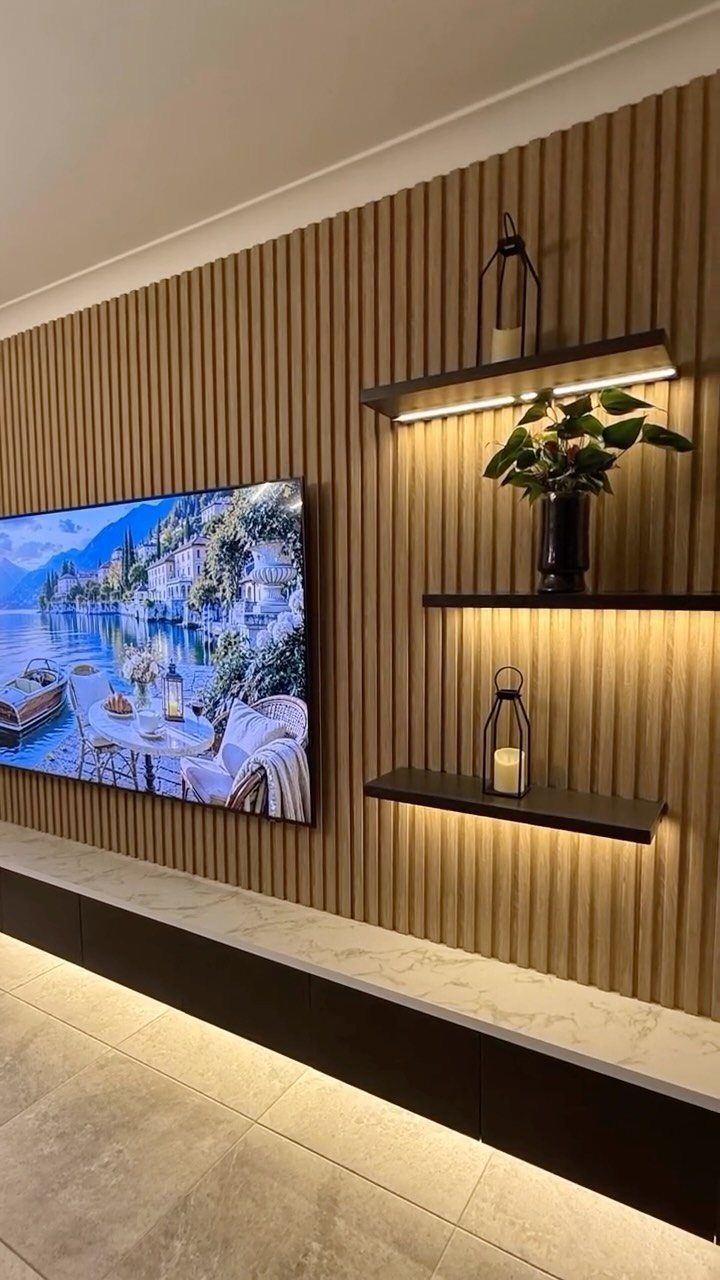 Recessed TV on a wall with vertical wooden slats and illuminated floating shelves.