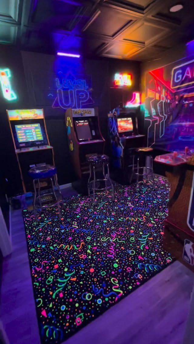 Three arcade game cabinets in a dark room with neon signs and colorful carpet.