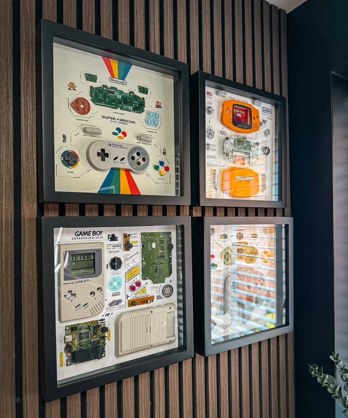 Disassembled retro handheld game consoles displayed in four black shadow boxes on a wooden wall.