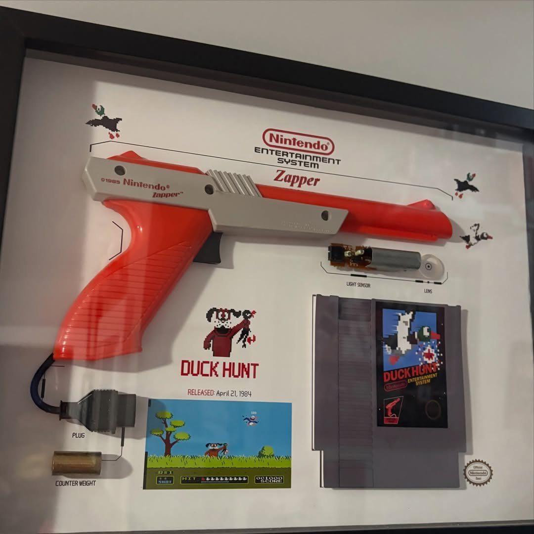 Framed shadow box display featuring a Nintendo Zapper gun and Duck Hunt game cartridge.