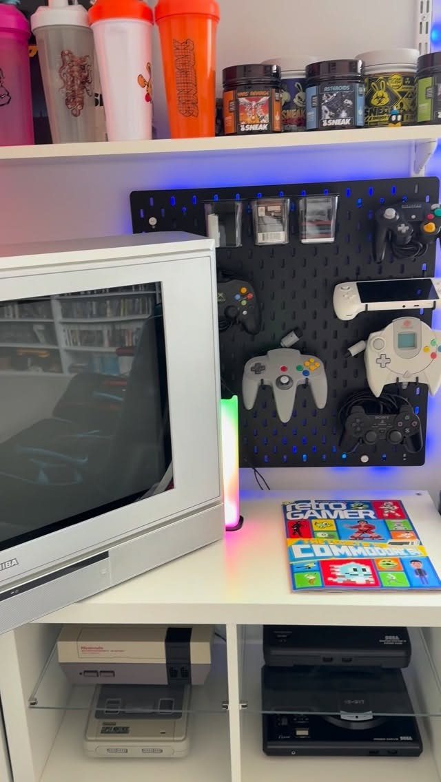 Retro gaming setup with CRT television, consoles, and controllers on a pegboard.
