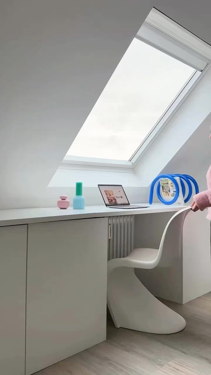 White attic workspace with a skylight, built-in desk, and modern white plastic chair.