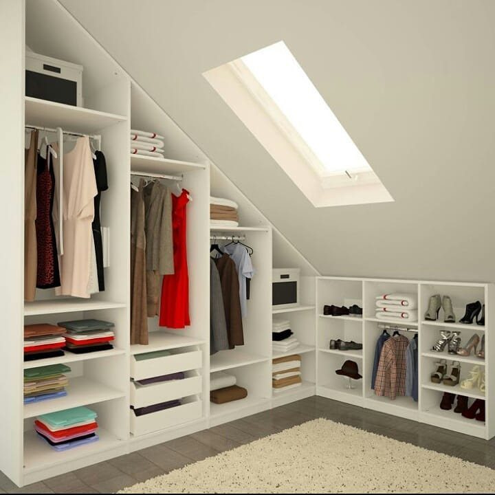 White built-in wardrobe with hanging clothes and shelves integrated into sloped attic eaves.