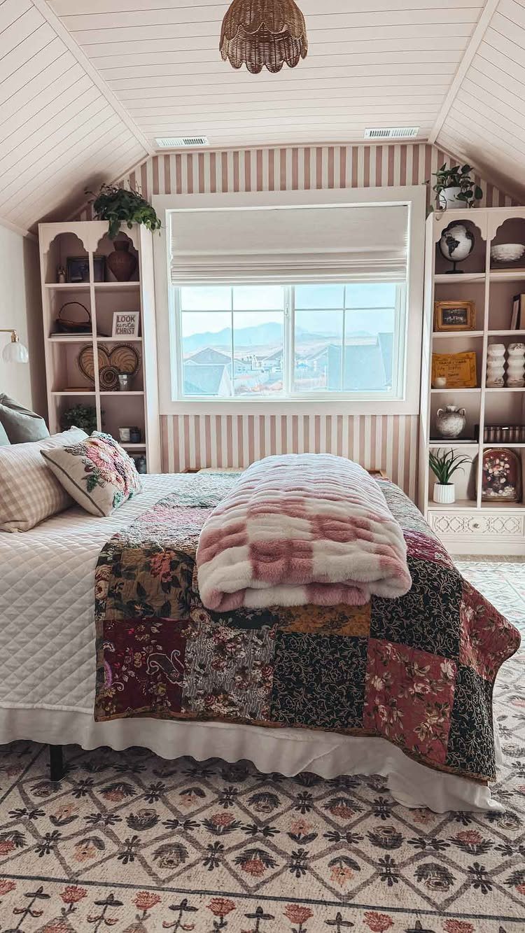Attic bedroom with patchwork quilt, striped wallpaper, and white built-in bookshelves.