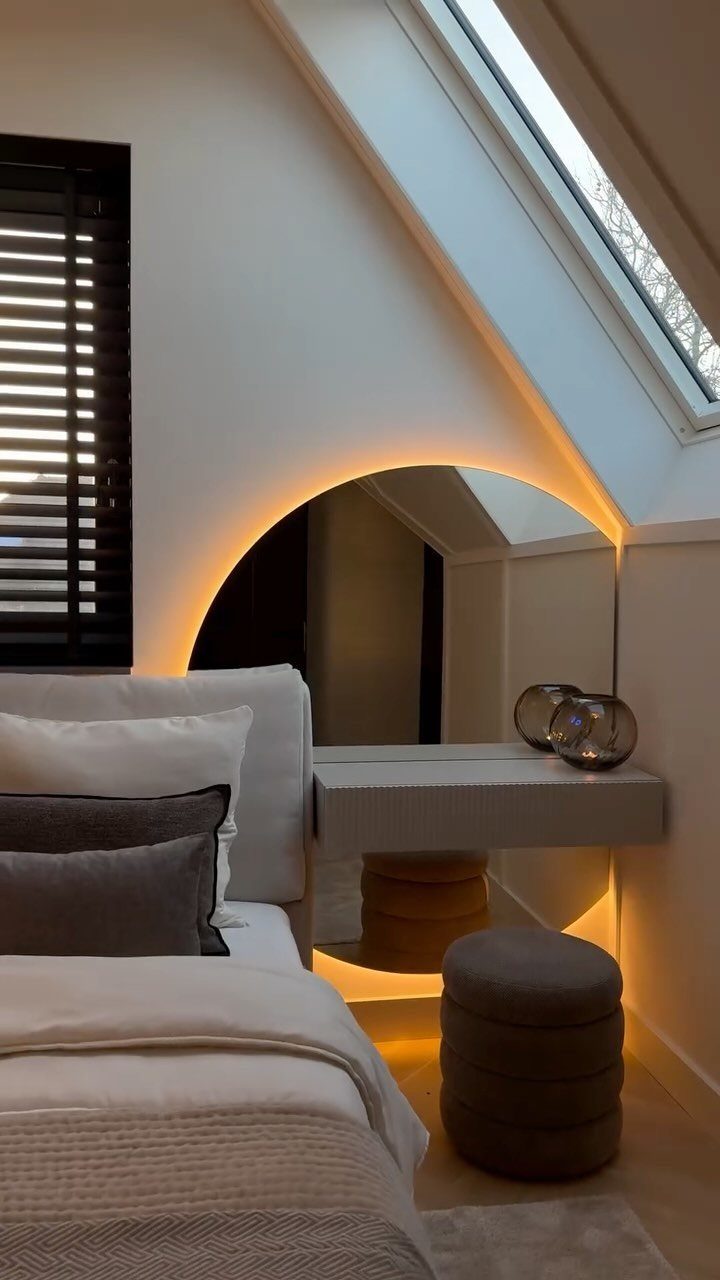 Small attic bedroom with a floating vanity desk, arched backlit mirror, and grey stool.