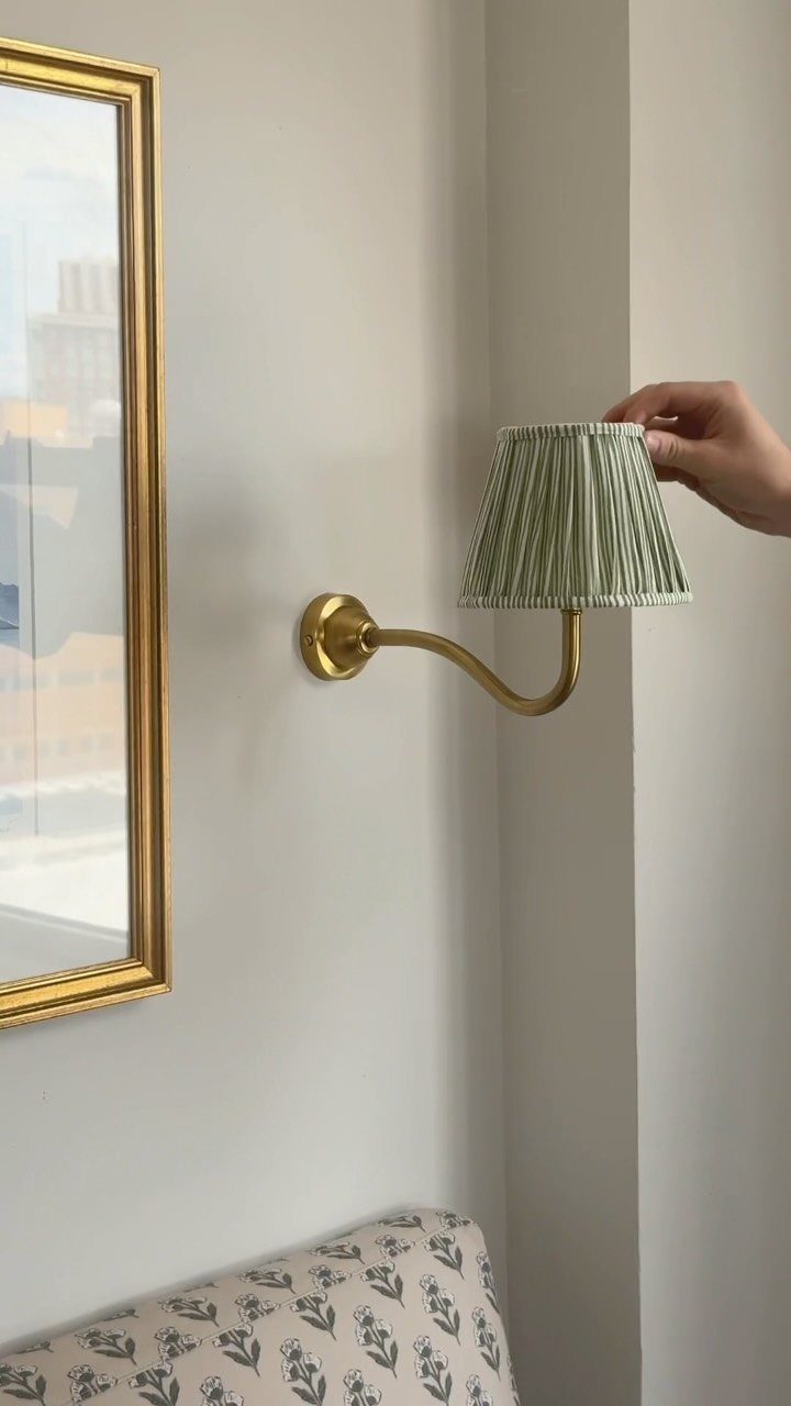 Gold wall-mounted sconce with a pleated green shade next to a gold mirror