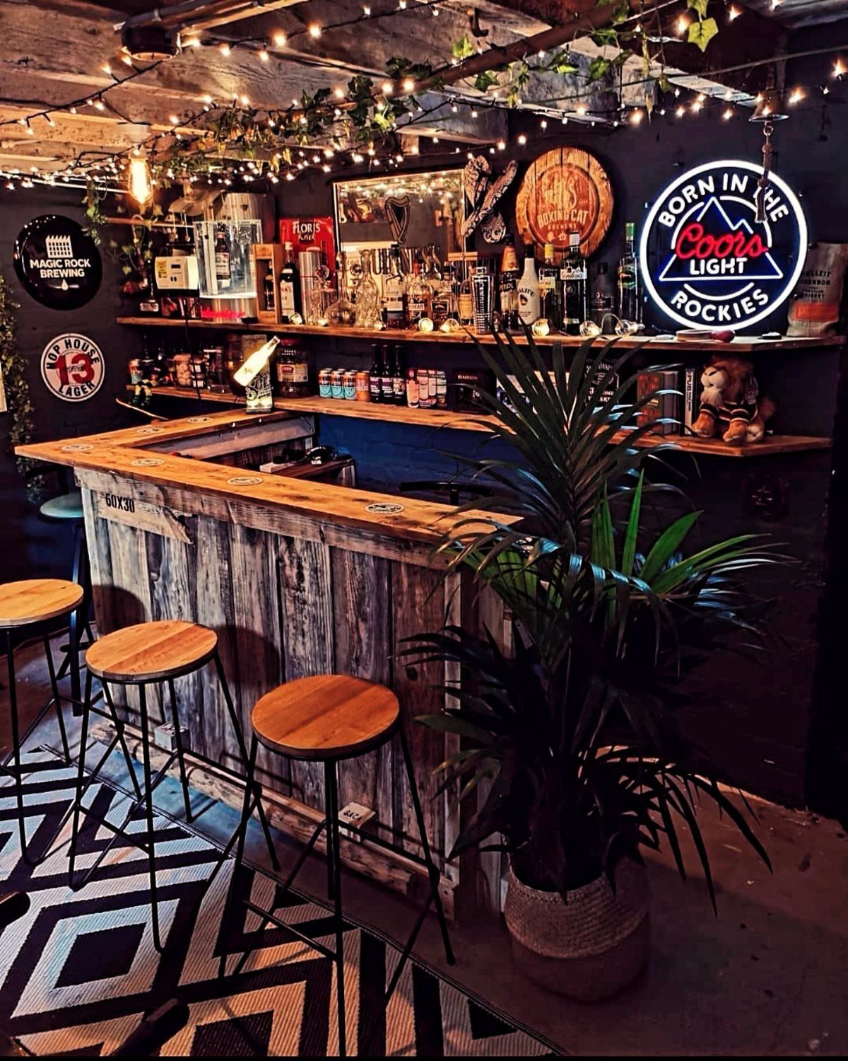 18 Small Bars for Home That Fit Any Space 11 Rustic L-shaped weathered wood home bar with stools and decorative string lights.