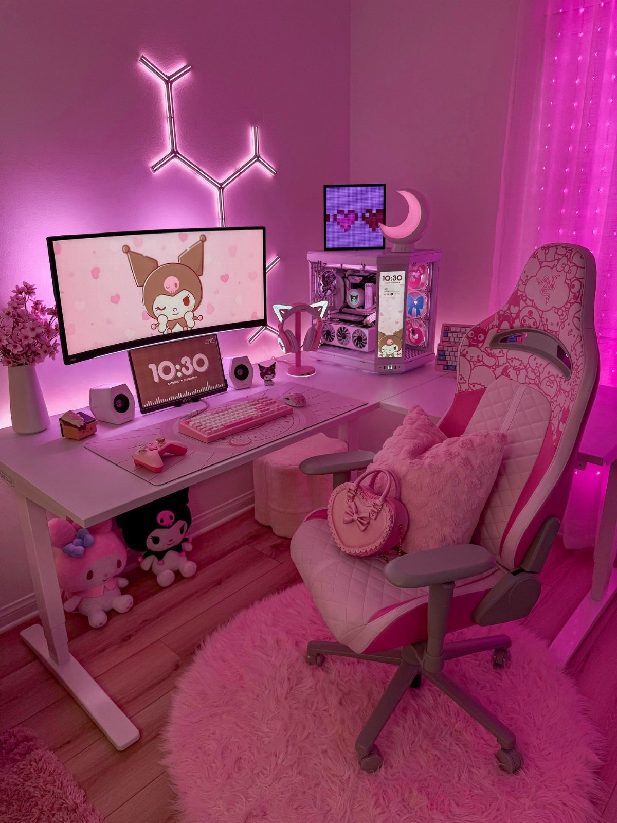Pink gaming setup with white desk, pink gaming chair, and fluffy pink rug.