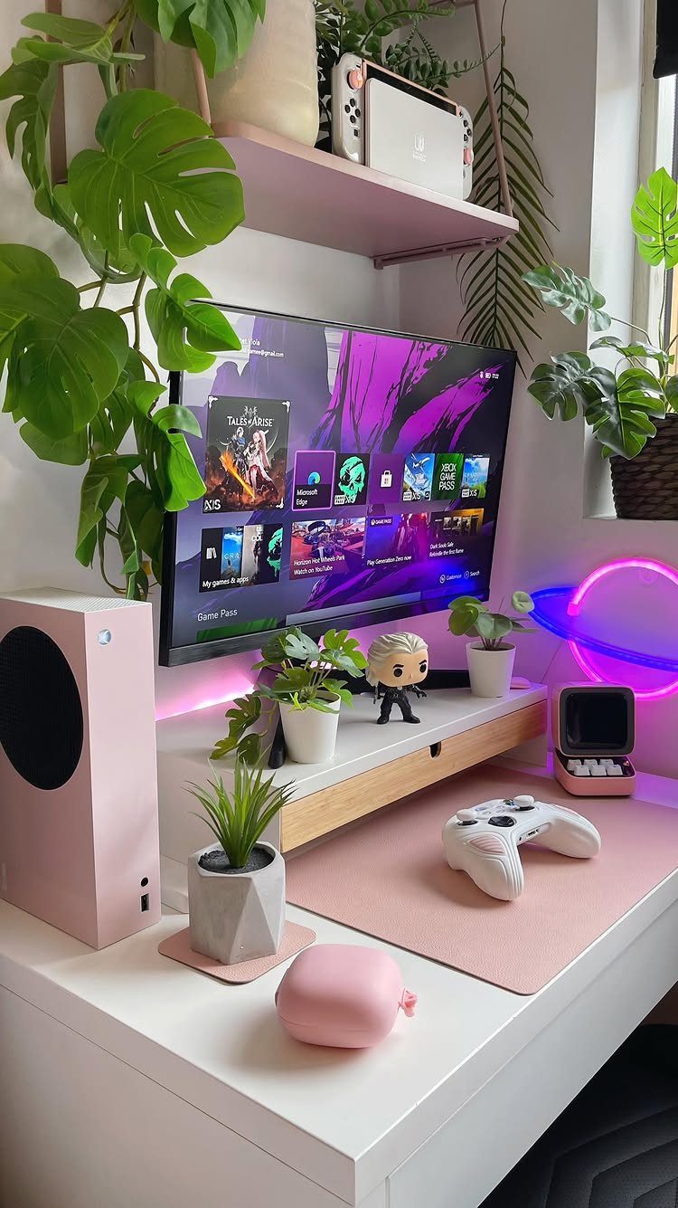 Pink and white gaming setup with a monitor, plants, and neon circular lighting.