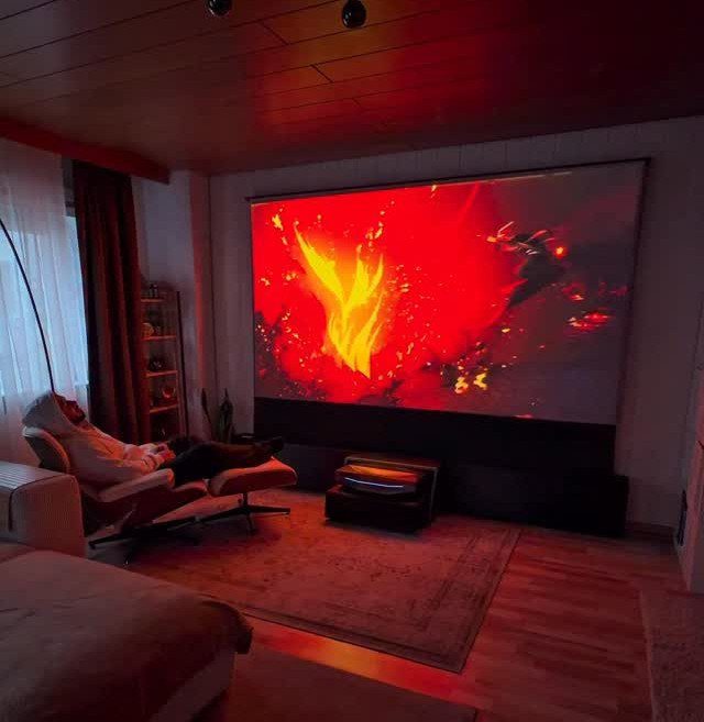 Large projection screen displaying fire in a dimly lit room with a lounge chair.
