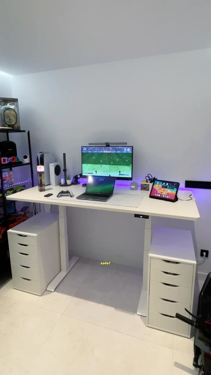 White gaming desk with monitor, laptop, and tablet between two white drawer units.