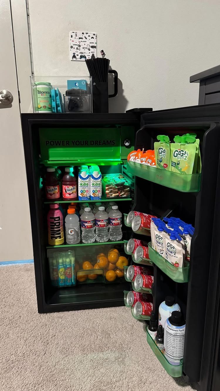 Open black mini-fridge stocked with sports drinks and snacks in a room.
