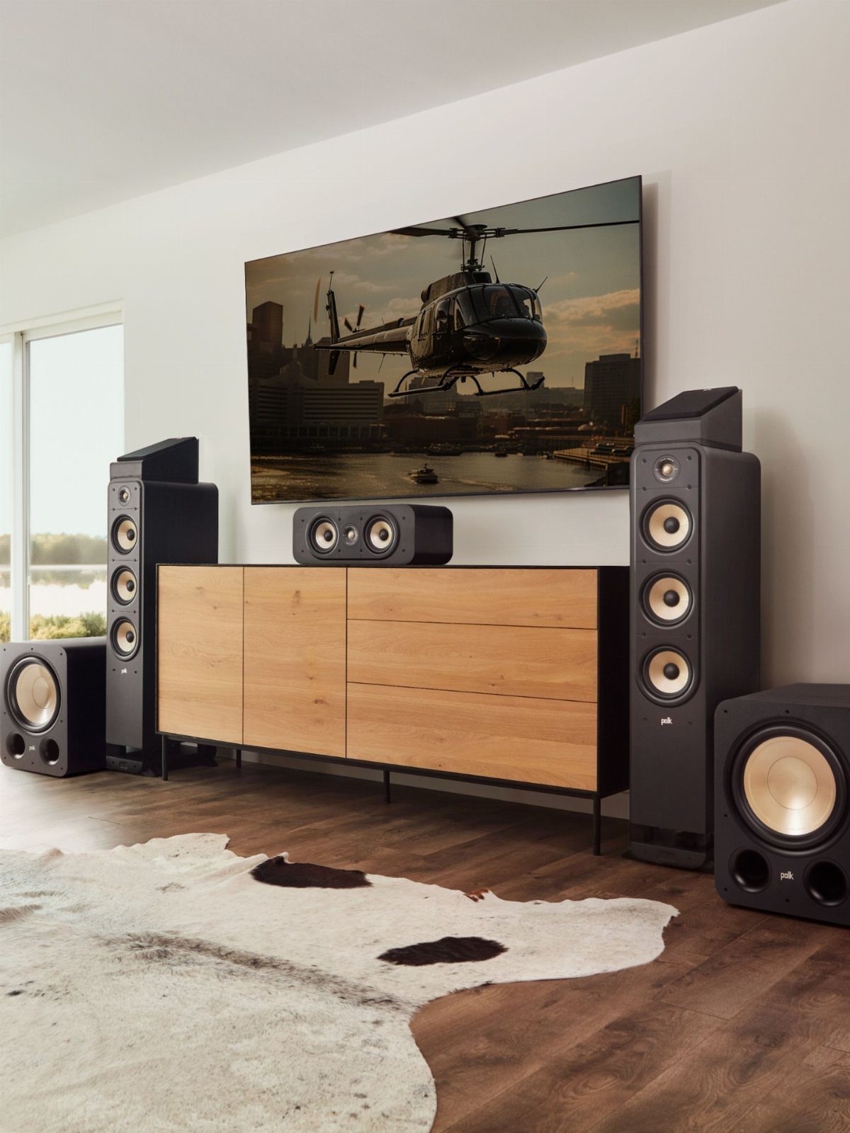 Home media setup with large television, black speakers, and wooden console on cowhide rug.