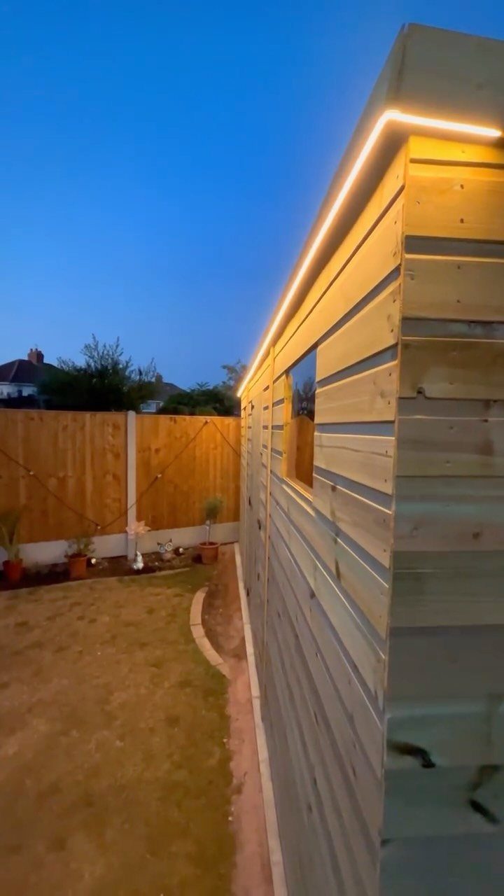 Wooden garden shed with warm LED strip lighting along the roofline at dusk.