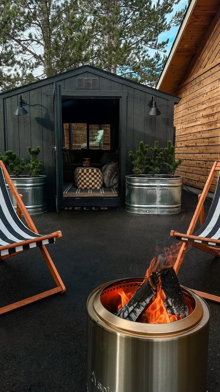 Black converted shed lounge with outdoor fire pit and striped deck chairs.