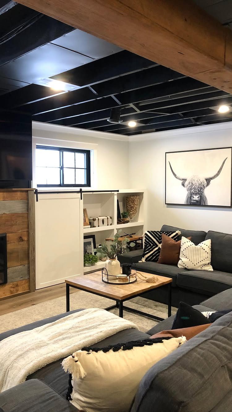Black painted unfinished basement ceiling with exposed joists in a modern living room.
