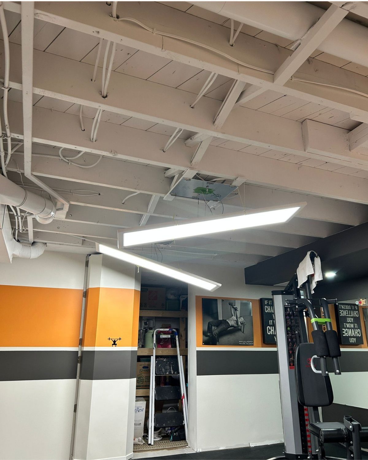 White painted unfinished basement ceiling with exposed joists above a home gym area.