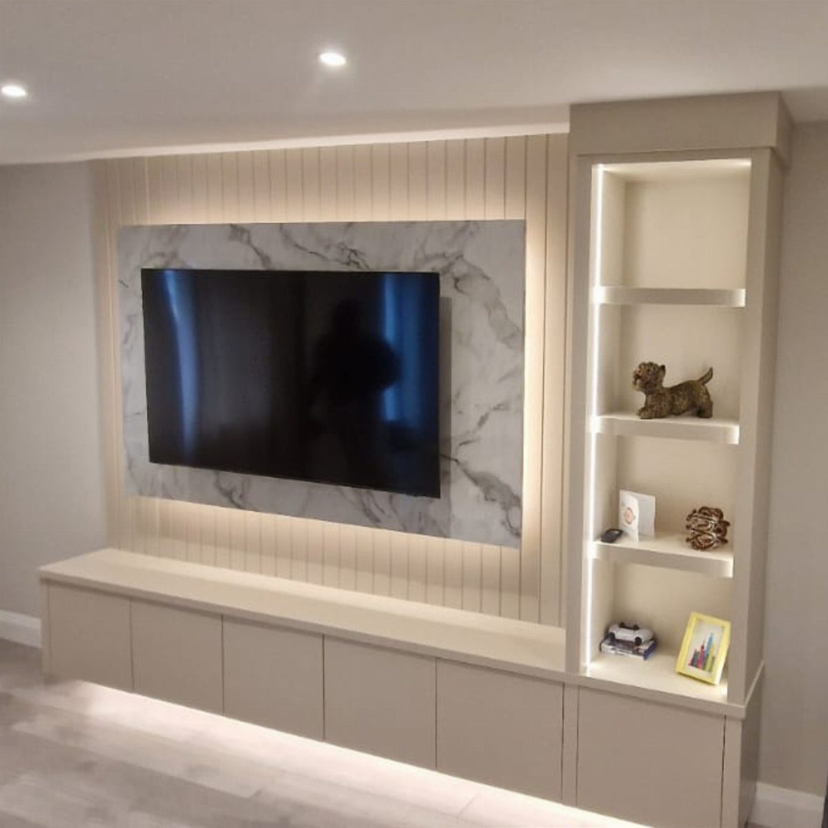 Modern asymmetrical wall TV unit with marble panel and illuminated side shelving.
