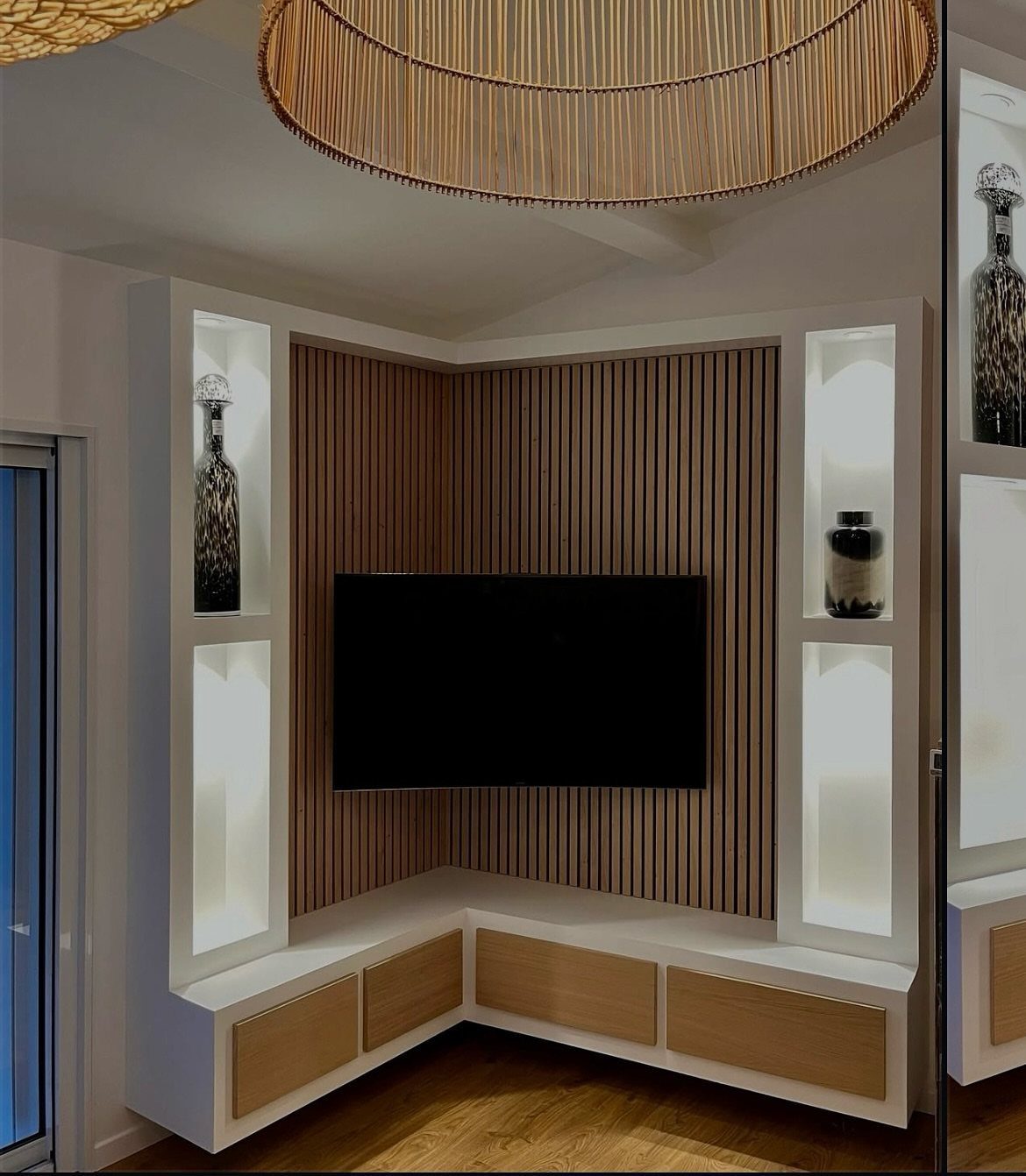 Corner TV unit with wood slat wall, white cabinets, and illuminated display shelves.