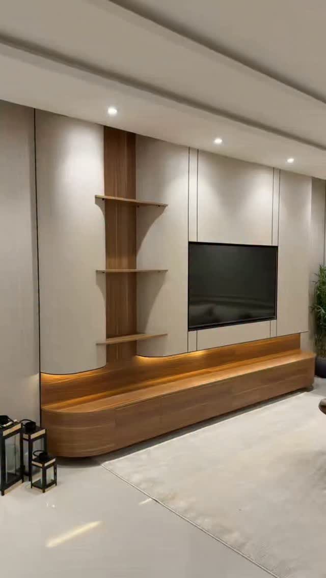 Modern TV unit with a curved wooden base and floating shelves on a paneled wall.