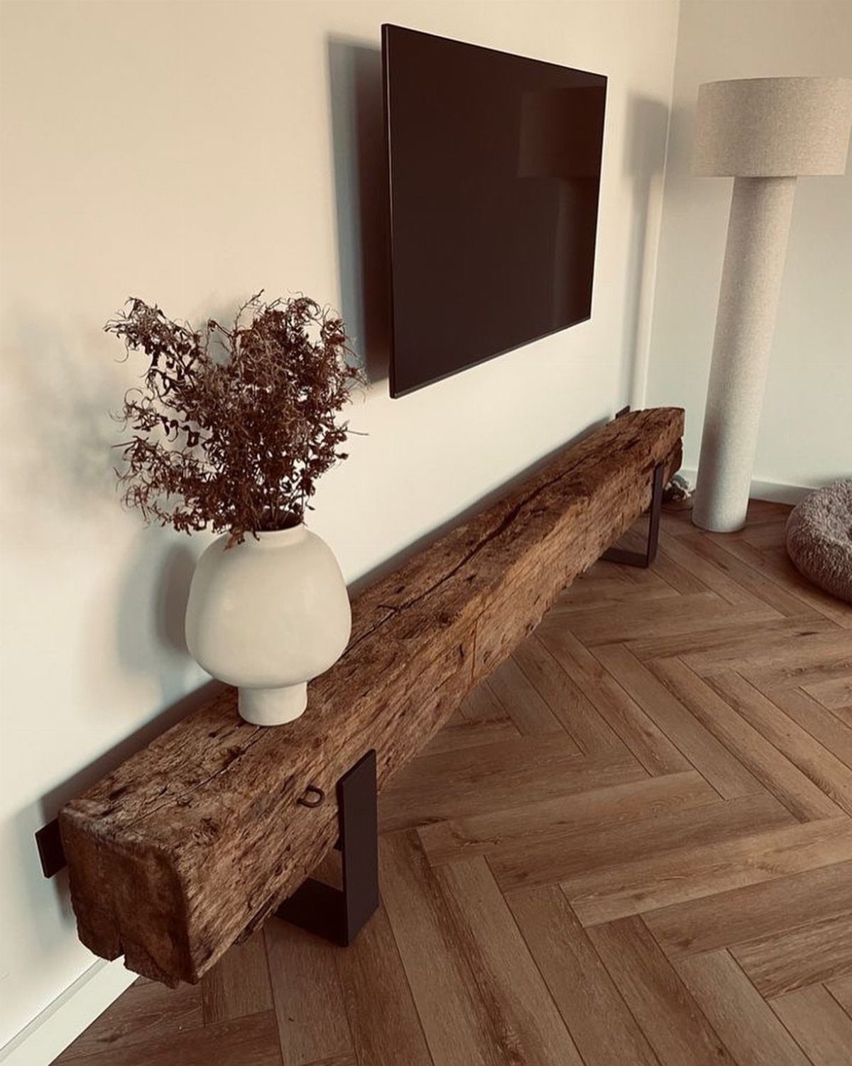 Rustic reclaimed wooden beam TV stand with a wall-mounted television and white vase.