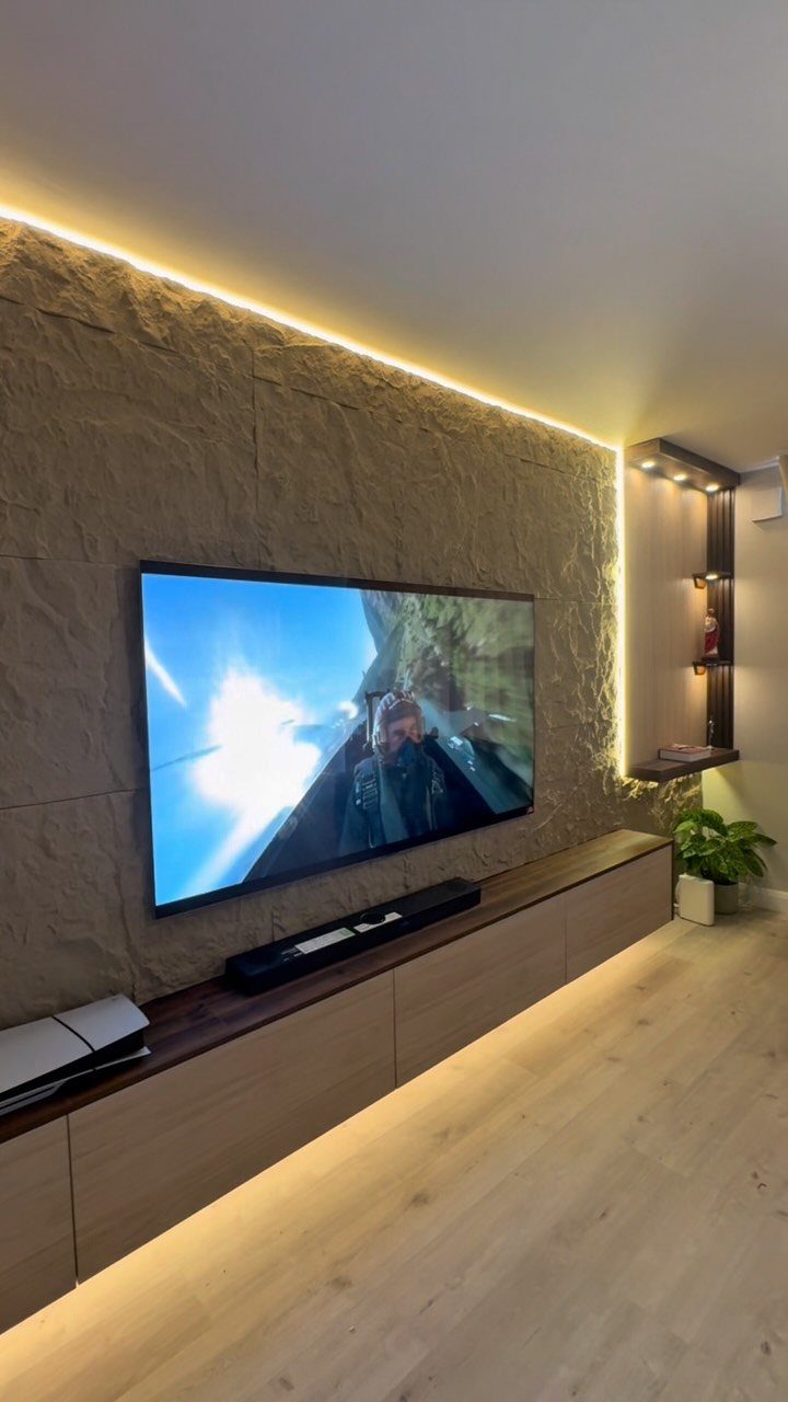 Television mounted on a textured stone wall with a long wooden floating console below.