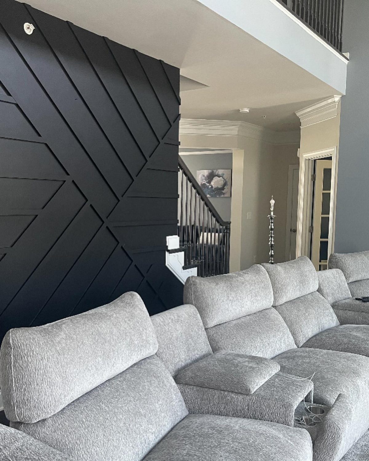 Black geometric wood slat accent wall behind light gray theater seating.